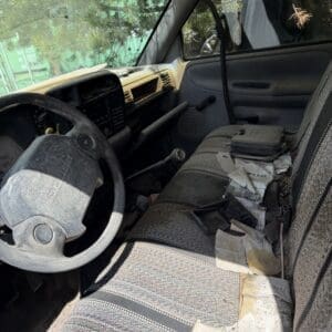 IMG_6802 - Montana Auctions by Kevin Hill Interior of a dusty, worn pickup truck with a cluttered bench seat, steering wheel, and scattered papers and debris on the passenger side.