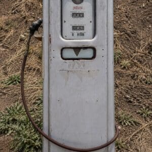 IMG_6806 - Montana Auctions by Kevin Hill Antique metal gas pump with a long rubber hose in a barren, rocky yard.