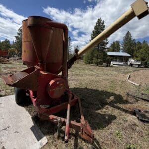 IMG_6813 - Montana Auctions by Kevin Hill Rusty red New Holland grain mixer on a trailer in a rural yard with trees in the background