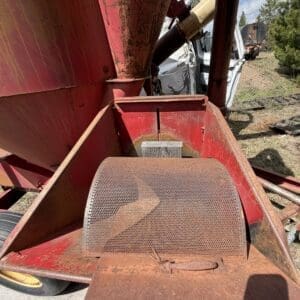 IMG_6814 - Montana Auctions by Kevin Hill Close-up of a rusty red farm machine with a perforated metal guard and weathered surfaces outdoors on a sunny day.
