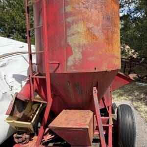 IMG_6815 - Montana Auctions by Kevin Hill Red, rusty cylindrical grain bin mounted on a trailer with a metal ladder along the side, outdoors in a yard.