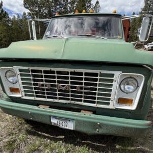 IMG_6821 - Montana Auctions by Kevin Hill Front view of a weathered green GMC truck with rusted grille parked on a dirt lot, overgrown grass nearby.