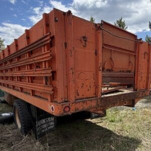 IMG_6823 - Montana Auctions by Kevin Hill Rusted orange dump trailer with side slats parked on a grassy lot, a spare tire nearby and trees in the background