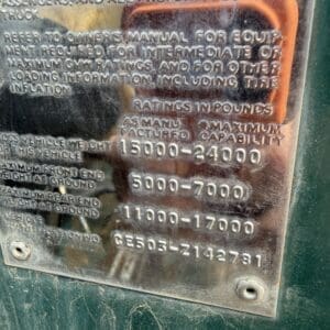IMG_6825 - Montana Auctions by Kevin Hill Metal vehicle information plate with weight ratings and inflation data mounted on a green surface; shows 15000-24000, 5000-7000, 11000-17000 and a serial/VIN number.