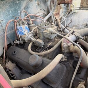 IMG_6827 - Montana Auctions by Kevin Hill Old, dusty car engine with rusted components, exposed hoses and a carburetor in a weathered engine bay of a neglected vehicle.
