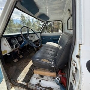 IMG_6831 - Montana Auctions by Kevin Hill Interior of an old pickup truck: blue dashboard, worn gray bench seat, and rust on the door frame and floor.