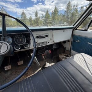 IMG_6834 - Montana Auctions by Kevin Hill Interior of a vintage blue-and-white car showing the dashboard, steering wheel, and bench seat with a forest view through the windshield