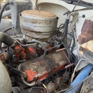 IMG_6835 - Montana Auctions by Kevin Hill Rusty vintage car engine with a round air filter on top and peeling orange paint in a dusty engine bay.
