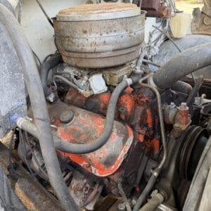 IMG_6836 - Montana Auctions by Kevin Hill Rusty round air filter housing atop a dusty, orange engine in a vintage truck bay with cracked paint and hoses.
