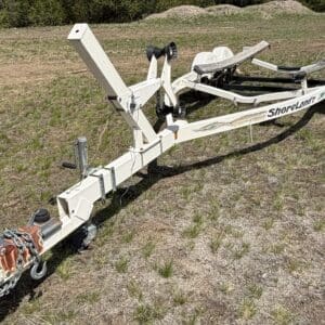 IMG_6839 - Montana Auctions by Kevin Hill White ShoreLand’r boat trailer parked on a grassy field, showing hitch, winch, and bunk supports.