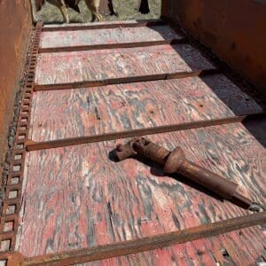 IMG_6844 - Montana Auctions by Kevin Hill Old rusted farm trailer bed with peeling red paint and a detached hitch lying on its surface; cows visible in the background.