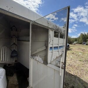 IMG_6853 - Montana Auctions by Kevin Hill Open white horse trailer with rust and dirt; interior shelves and gear visible on a sunny rural field.