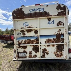 IMG_6854 - Montana Auctions by Kevin Hill Rear view of a rusted white bus with 'CANYON' on top, peeling paint and heavy rust, parked on a grassy lot against a blue sky.