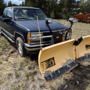IMG_6858 - Montana Auctions by Kevin Hill Blue pickup truck with a large yellow Meyer snow plow attached, parked in a muddy field with trees in the background.