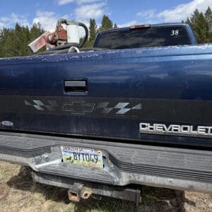 IMG_6860 - Montana Auctions by Kevin Hill Blue Chevrolet pickup truck viewed from the rear with a dusty bumper, a Montana license plate, and a red tool mounted on the bed rail behind the cab.