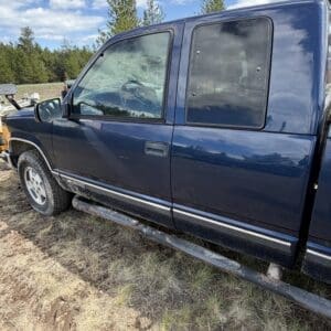 IMG_6861 - Montana Auctions by Kevin Hill Blue pickup truck with running boards parked on dry grass; cracked passenger-side window in the cab area.