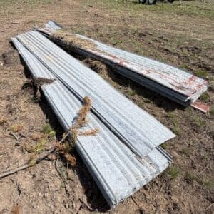 IMG_6868 - Montana Auctions by Kevin Hill Stacked corrugated metal roofing sheets on dirt, with a trailer in the background at an outdoor work site.
