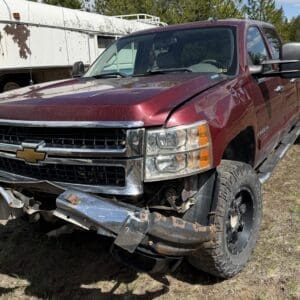 IMG_6871 - Montana Auctions by Kevin Hill Red Chevrolet pickup with significant front-end damage and crumpled bumper on a grassy lot, towing-ready.