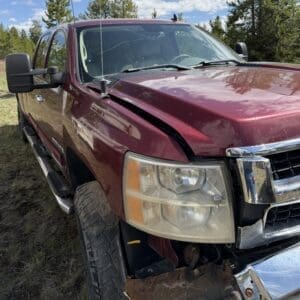 IMG_6872 - Montana Auctions by Kevin Hill Maroon pickup truck with a dented hood and rusted front bumper in a grassy area, showing damage to the left front side of the vehicle to the camera.