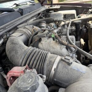 IMG_6874 - Montana Auctions by Kevin Hill Open hood view of a dusty engine bay, featuring a large ribbed air intake hose and exposed wiring.