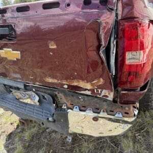 IMG_6877 - Montana Auctions by Kevin Hill Red Chevrolet pickup with severe rear-end damage, crushed tailgate, and missing bumper in a grassy, outdoor area.
