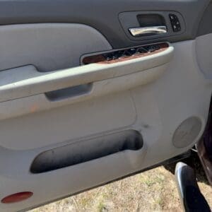 IMG_6878 - Montana Auctions by Kevin Hill Interior of a car door panel with a chrome handle, wood trim and window/lock controls, plus a lower storage pocket and speaker grille.