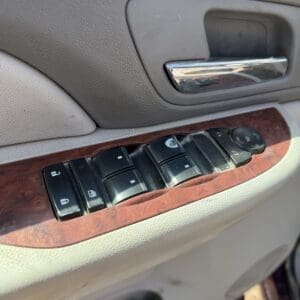 IMG_6879 - Montana Auctions by Kevin Hill Car door interior with chrome handle, wood trim, and four power window buttons on a beige panel.