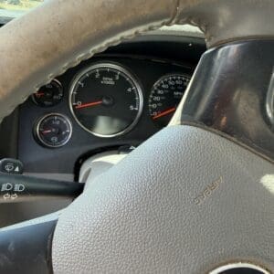 IMG_6881 - Montana Auctions by Kevin Hill Driver's cockpit view of a car dashboard showing RPM and speedometers behind a worn leather steering wheel.