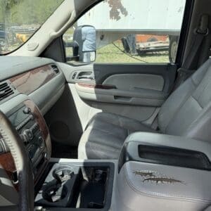 IMG_6883 - Montana Auctions by Kevin Hill Interior view of a gray pickup truck front cabin with a cracked center armrest, cup holders, and wood trim; a trailer is visible outside the passenger window.