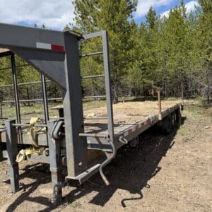 IMG_6885 - Montana Auctions by Kevin Hill Flatbed trailer with a rusted metal frame in a dirt lot, pine trees in the background and a blue sky above.