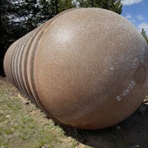 IMG_6889 - Montana Auctions by Kevin Hill Large rust-colored spherical metal tank lying on its side in an outdoor yard, with trees in the background.