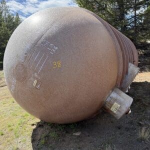 IMG_6890 - Montana Auctions by Kevin Hill Large rusty spherical tank lying on its side outdoors, with trees and a clear sky in the background.