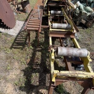 IMG_6893 - Montana Auctions by Kevin Hill Old rusty conveyor-like rollers and yellow frame in a sunny outdoor scrap yard with various metal parts nearby.