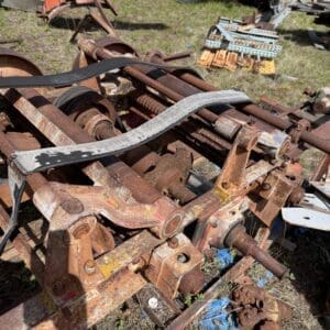 IMG_6894 - Montana Auctions by Kevin Hill Rusty metal frame and gears from old agricultural machinery in a junkyard, with pallets and scrap scattered nearby.