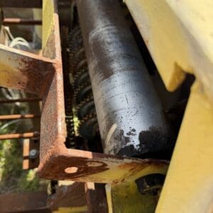 IMG_6895 - Montana Auctions by Kevin Hill Close-up of a rusted metal frame with a large black cylindrical rod and visible gears in the background, part of industrial machinery.