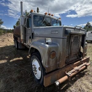 IMG_6897 - Montana Auctions by Kevin Hill A rusted International 4200 semi-truck in a rural yard, front grill damaged and rusted, with dirt and piles in the background.