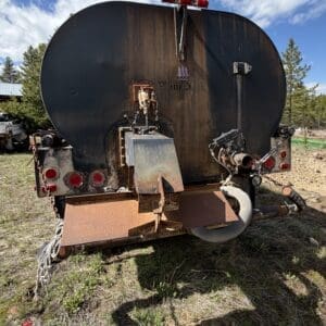 IMG_6899 - Montana Auctions by Kevin Hill Rear view of a large, rusted cylindrical tanker trailer with red taillights and metal attachments in a dirt lot.