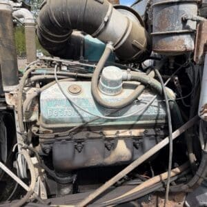 IMG_6906 - Montana Auctions by Kevin Hill Close-up of a dusty Detroit Diesel engine with a large curved air intake tube, rusted metal components, and tangled hoses in a truck engine bay.