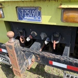 IMG_6911 - Montana Auctions by Kevin Hill Rear view of a lime-green truck/trailer with a rusty hitch and Montana license plate visible, showing connectors and taillights above a metal step.