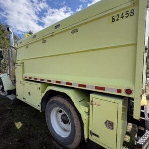 IMG_6913 - Montana Auctions by Kevin Hill Rear/side view of a yellow utility dump truck with a large cargo bed, storage compartments, and a single wheel visible; number 62458 on the side.
