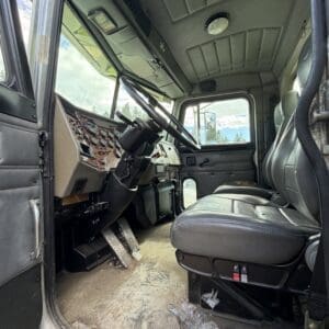 IMG_6914 - Montana Auctions by Kevin Hill Interior of a dirty, older truck cab with the driver's seat, steering wheel, and a dusty floor; tools scattered on the floor near the doorway.