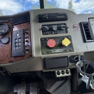 IMG_6917 - Montana Auctions by Kevin Hill Close-up of a truck dash showing the red trailer air supply knob and yellow control cap, with dashboard gauges and a cup holder nearby.