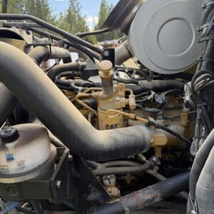 IMG_6919 - Montana Auctions by Kevin Hill Close-up of a heavy diesel engine bay with yellow CAT pump, thick hoses, and metal fittings on rugged equipment.
