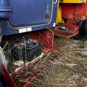 Blue truck cab with exposed battery and wiring on a red undercarriage, parked on frost-dusted grass.