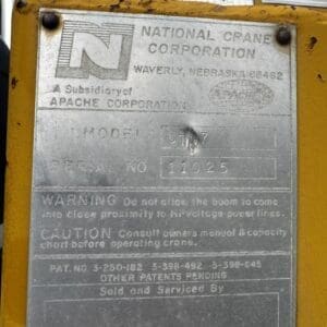 Metal nameplate on a yellow crane with model and serial numbers and safety warnings from National Crane Corporation (Apache subsidiary).