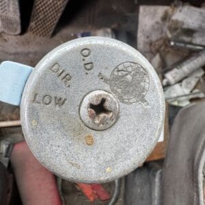 Round dusty metal cap with a central Phillips screw; appears to be a fuel or oil cap on a weathered machine.