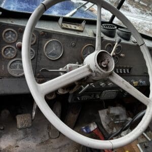 Old, dusty vintage truck interior with a large white steering wheel and weathered dashboard gauges.