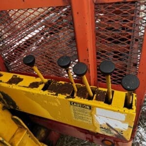 Close-up of yellow control panel with four black knob levers on a rusted orange industrial machine outdoors.