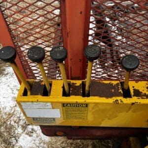 Five black-knob levers on a yellow control panel of rusted orange industrial equipment, outdoors in snow. Includes caution labels and a grated back panel.