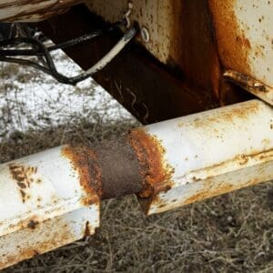 Close-up of a white, rusted metal beam and pipe junction with heavy orange rust and peeling paint outdoors.